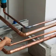 Ręce fachowca wykonują lutowanie twarde miedzianych rur instalacji.