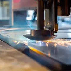 Głowica tnąca laserem przecina metalową płytę, tworząc iskry i dym.