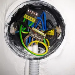 Wnętrze puszki instalacyjnej z przewodami: niebieskim, zielono-żółtym i czarnym, połączonymi złączkami. Trwa zerowanie gniazdka.