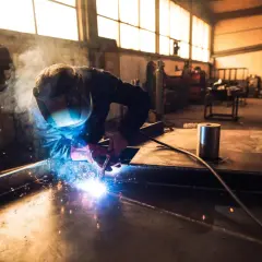 Spawacz w masce ochronnej spawa metal, tworząc jasne iskry i dym w warsztacie.