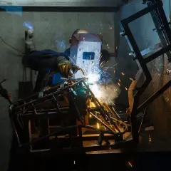Spawacz w masce tworzy konstrukcję, iskry sypią się wokół. Czy to spawanie aluminium AC czy DC?
