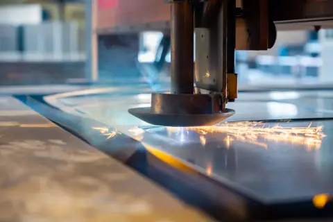 Głowica tnąca laserem przecina metalową płytę, tworząc iskry i dym.