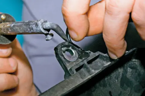 Ręce trzymają lutownicę i element z tworzywa sztucznego, wykonując spawanie plastiku.
