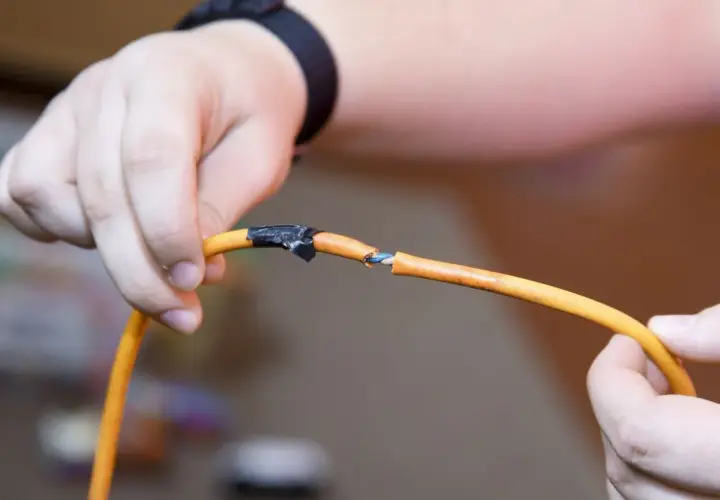 Dłonie trzymają przerwany pomarańczowy kabel, odsłaniając niebieskie przewody. Jak sprawdzić w którym miejscu jest przerwany kabel?