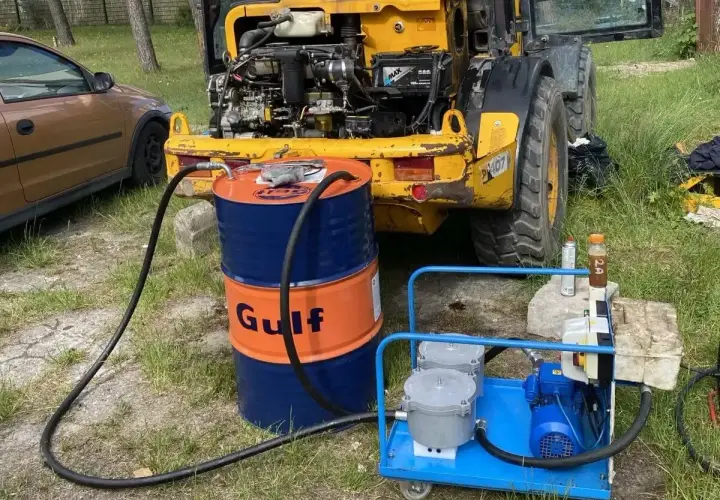 Niski poziom oleju hydraulicznego objawy: maszyna budowlana z otwartą maską, beczka Gulf, pompa.