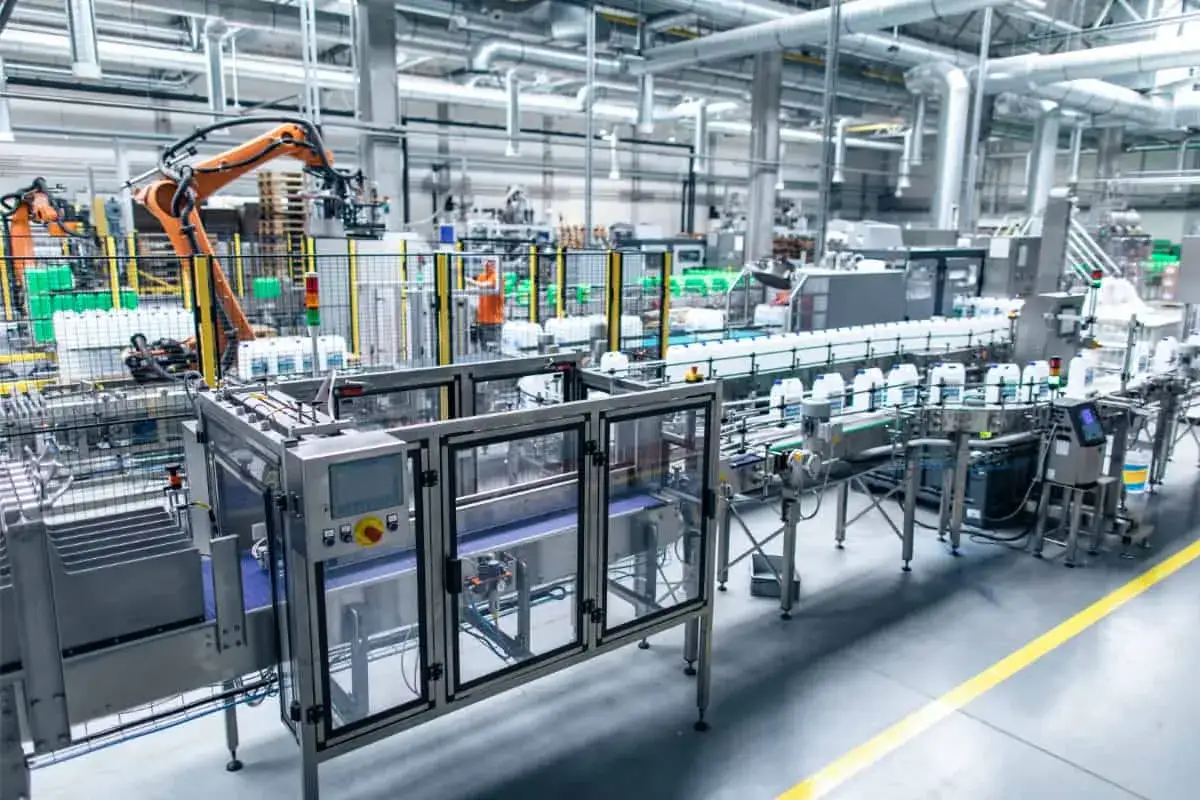 Nowoczesna linia produkcyjna z robotami i czujnikami przemysłowymi, gdzie butelki z płynem przemieszczają się na taśmociągu.